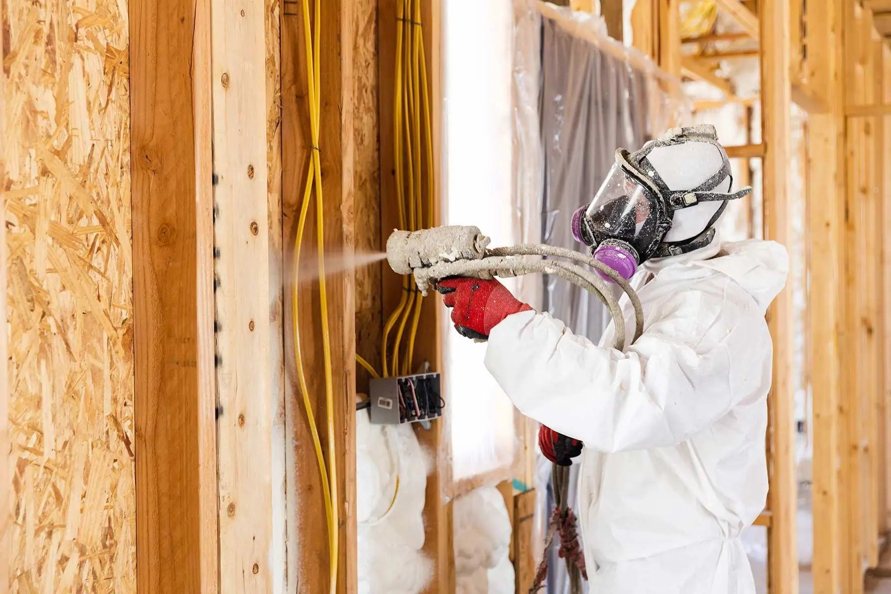 Technician spraying foam insulation on framed walls